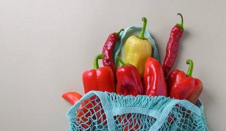 Zero waste concept. Various colorful peppers in turquoise string mesh bag on light background, Copy...