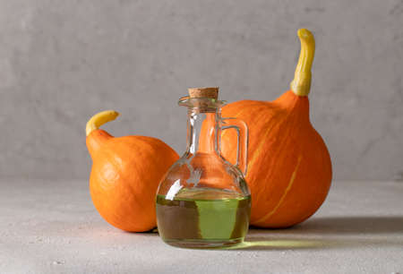 Pumpkin oil in a bottle and two bright pumpkins on light gray background, Closeupの写真素材