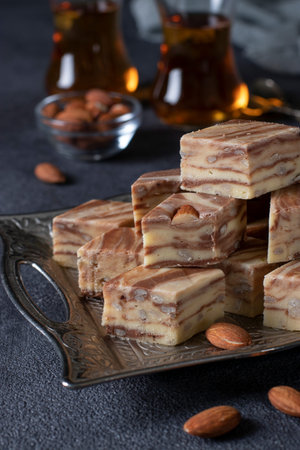 Delicious slices of Oriental milk halva with almonds and cocoa on dark gray background. Uzbek...