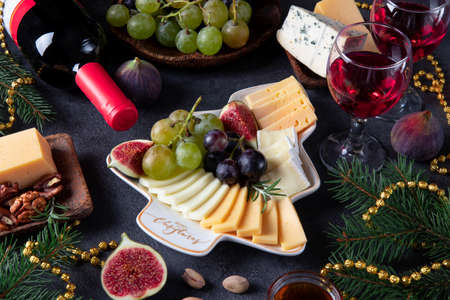 Variety of cheese and fruits served in plate as Christmas tree, on dark gray background with two glasses of wine. New Year's Eve Party Snackの写真素材