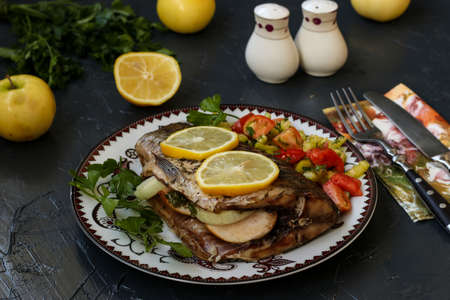 Baked fish on a plate with lemon, salad and greens.の写真素材