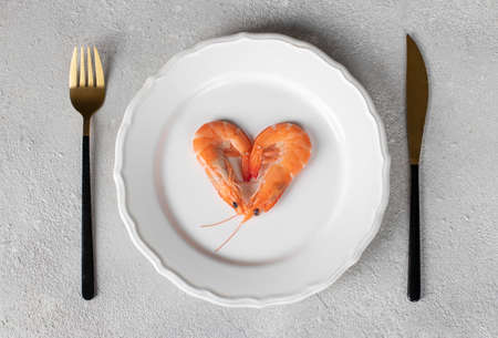 Two boiled shrimp in the shape of a heart on a round white plate on a light background, concept for Valentine's Day, Top viewの写真素材