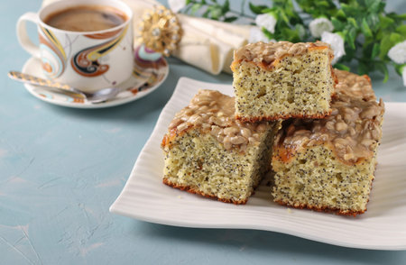Homemade sweet cake with poppy seeds, cut into slices on a plate on a light blue background,...