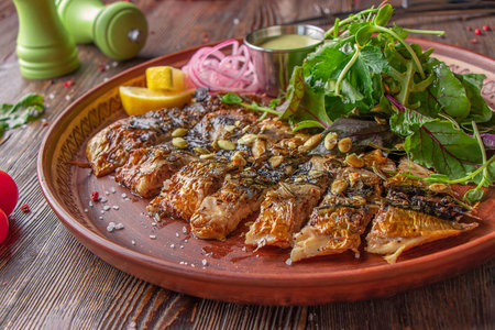 Grilled baked mackerel served with sauce, onion, lemon and green salad on wooden tableの写真素材