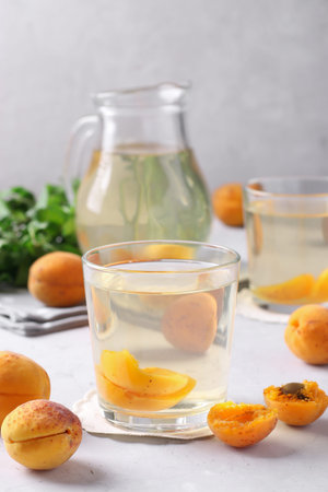 Homemade apricot compote in two glasses and jug on light gray background