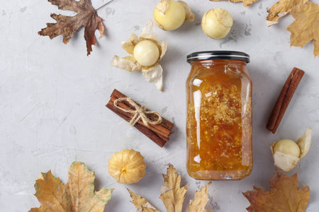 Homemade transparent physalis jam with cinnamon in glass jar on light gray background, Top view