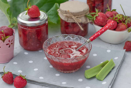 Homemade strawberry and rhubarb jam in bowl and glass jars on gray table in the gardenの写真素材