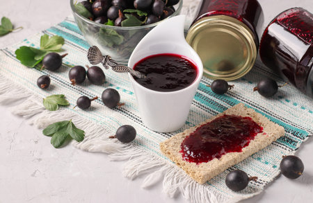 Homemade thick yoshta jam is spread on bread and served for breakfast, also jam in bowl and glass jarsの写真素材