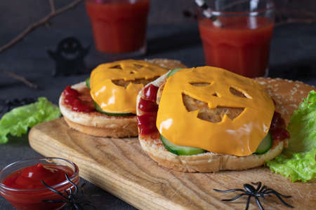 Two funny monster chicken burgers with toast cheese, ketchup and cucumber on wooden board. creative halloween foodの写真素材