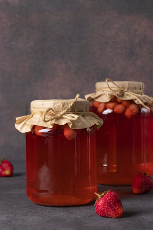Homemade canned compote with strawberries in two jars on brown background, Vertical formatの写真素材