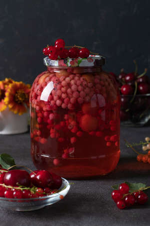 Homemade canned compote with sweet cherries and red currants in glass jar on dark gray background, Vertical formatの写真素材