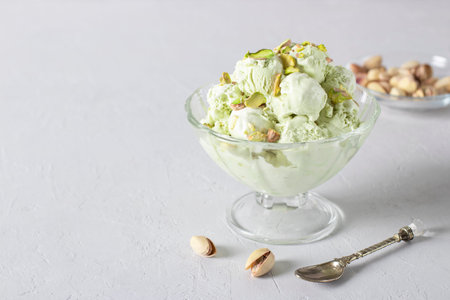 Pistachio ice cream with nuts in transparent glass ice-cream bowl on gray background, Copy space