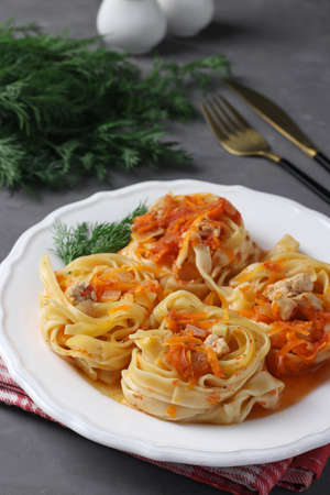 Tagliatelle pasta with turkey, vegetables and tomato sauce on a white plate on gray backgroundの写真素材