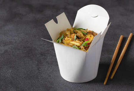 Noodles with seafood and vegetables in takeaway box on dark gray backgroundの写真素材