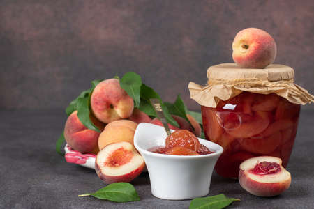 Homemade organic peach jam in glass jar and bowl on brown backgroundの写真素材