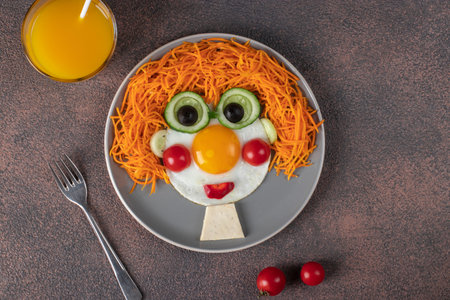 Fun Food for kids - smiling face ginger boy from fried eggs, carrot, cucumbers and cherry tomatoes...