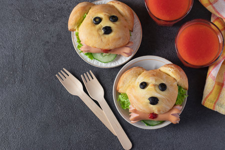 Fun food for kids - two sandwiches in the shape of dog with cucumber, sausages and tomato juice on dark gray background, Top viewの写真素材