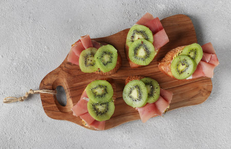 Sandwiches with soft cheese, prosciutto and kiwi on wooden board on light gray background, Top viewの写真素材