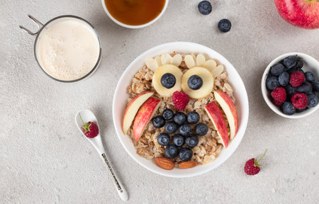 Cheerful breakfast for kids - sweet oatmeal in shaped owl with blueberries, raspberries, apple, honey and almondsの写真素材