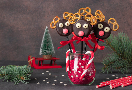 Cute idea for Christmas treats - cake pops Santas reindeers made from cookies in chocolate and crackers on brown backgroundの写真素材