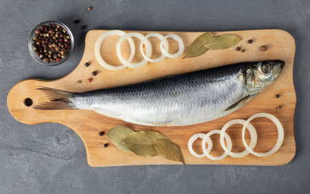 Salted herring with onion, peppers, sea salt and bay leaf on wooden board on dark gray background, Top viewの写真素材