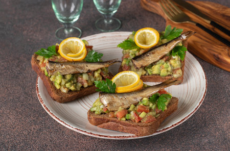 Homemade Guacamole sandwiches with sprats and lemon on plate on brown backgroundの写真素材