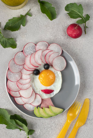 Fun Food for kids - smiling face made from fried eggs, radishes, olives and avocado. creative healthy breakfast for childrenの写真素材