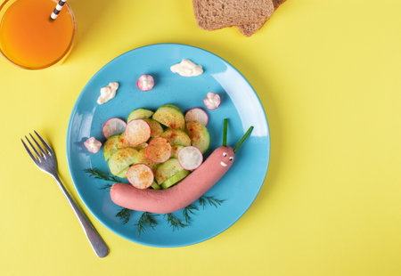 Idea breakfast for kids - funny snail from sausage with cucumber and radishes salad on a plate, Top viewの写真素材