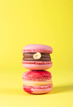 Two pink macarons with hazelnuts and caramel on yellow background, Vertical imageの写真素材