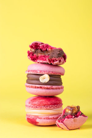 Pink macarons with hazelnuts and caramel on bright yellow background