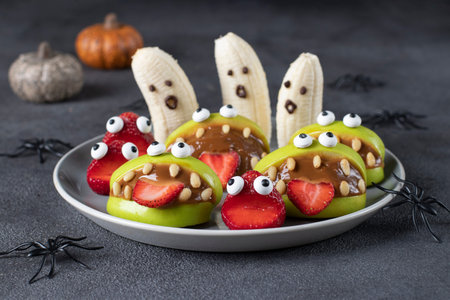 Spooky banana ghosts monsters, strawberry and green apple monsters for Halloween party on gray background decorated with spidersの写真素材