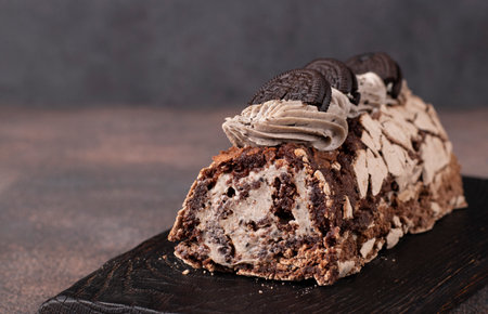 Chocolate meringue roll with cookies on a wooden board on dark gray backgroundの写真素材
