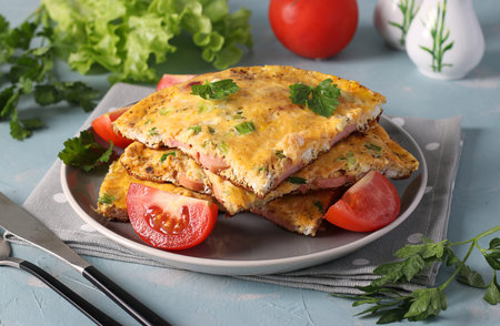 Omelet with sausages, cheese and parsley served with tomatoes on a gray plate on light blue...