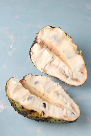 Two halves of ripe soursop on blue background, vertical format