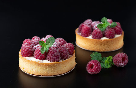 Tarts with fresh raspberries on a black background