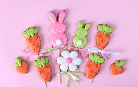 Easter gingerbread cookies in the shape of hare and carrots on pink background. Easter greeting...