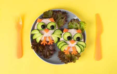 Sandwiches in shape of Owls for children with cucumber, carrots and olives, top view on yellow backgroundの写真素材