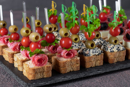 Assortment of canapes with cherry tomatoes, sausage, cheese, olives and seaweed caviar on slate plateの写真素材