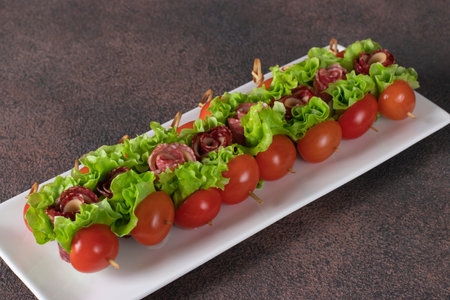 Canape with sausage, cheese, cherry tomatoes and lettuce leaves on white plateの写真素材