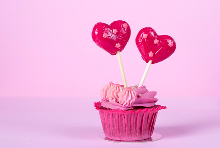 Cupcake with pink cream and heart lollipops on pink backgroundの写真素材
