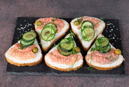 Sandwiches with salted salmon, olives and cucumber on slate plateの写真素材
