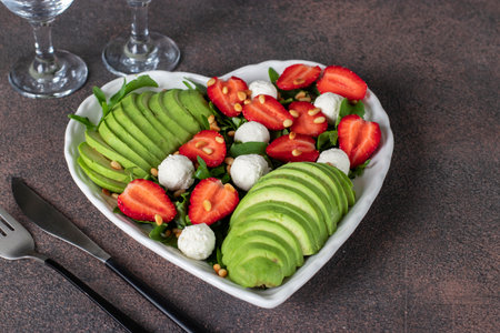 Healthy salad with strawberries, avocado, arugula and feta cheese in heart-shaped plate on brown backgroundの写真素材