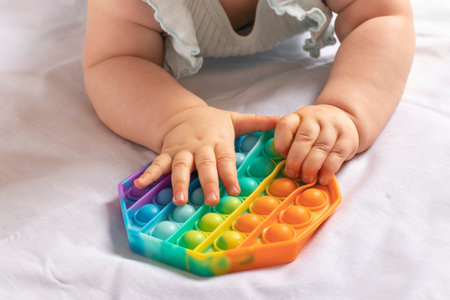 Newborn baby lies on his stomach playing trendy flexible silicone colorful toy Pop it