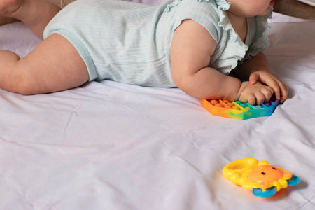 An eight-month-old child plays with colorful toys while lying on his stomach on bedの写真素材