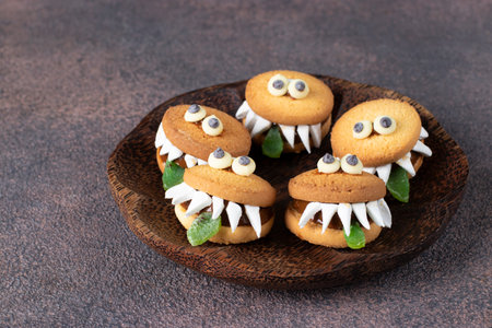 Halloween Party Treats - Cookie Monsters with Marshmallows, Condensed milk and Chocolate on wooden plateの写真素材