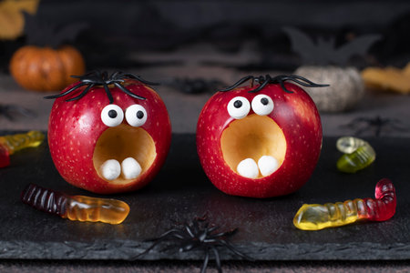 Red apple monsters for Halloween party on black plate decorated with spiders and wormsの写真素材