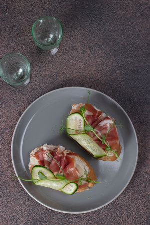 Sandwiches with cream cheese, jamon and cucumber on gray plate on brown backgroundの写真素材