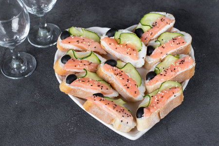 Sandwiches with salted salmon, black olives and cucumber on heart shaped plateの写真素材