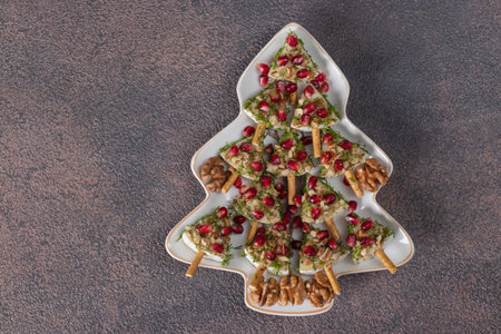 Appetizer of Brie cheese with pomegranate and walnuts in Christmas tree-shaped plate on brown...