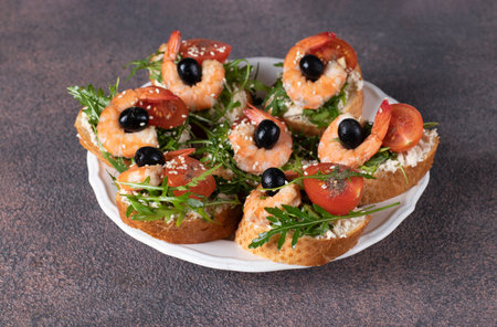 Bruschetta with shrimps, arugula, cream cheese and cherry tomatoes on white plateの写真素材